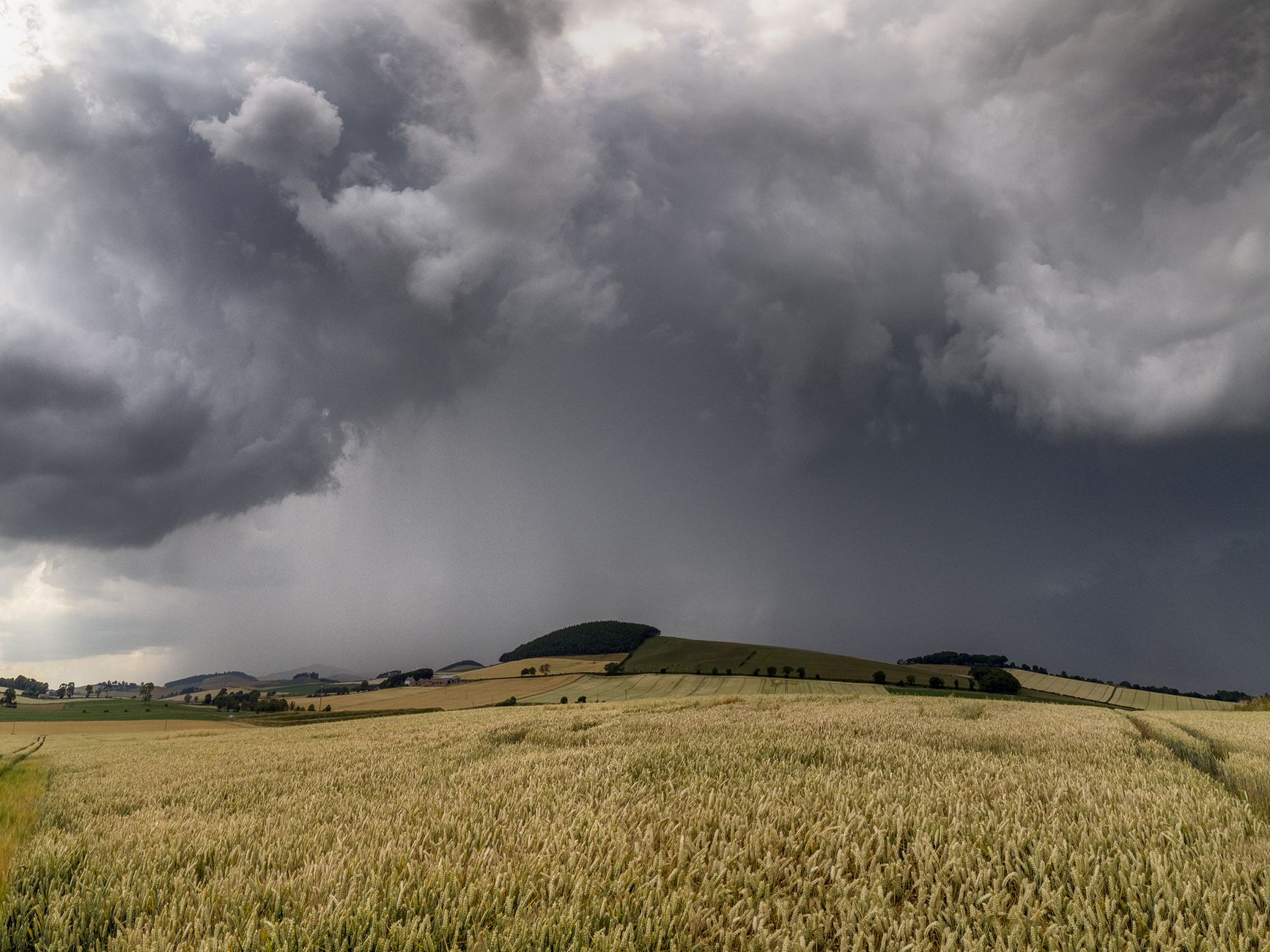 Dark storm clouds roiling across sky above a distant horizon with wind-swept landscape below.