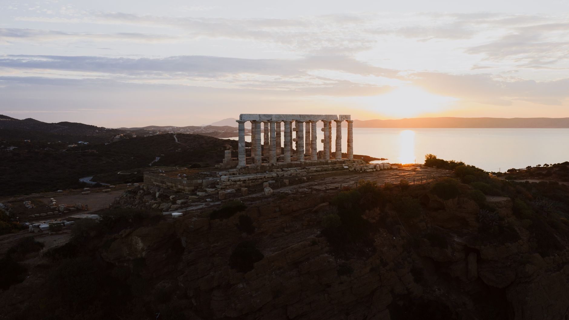 Weathered marble columns of an ancient Greek temple stand against a twilight sky.