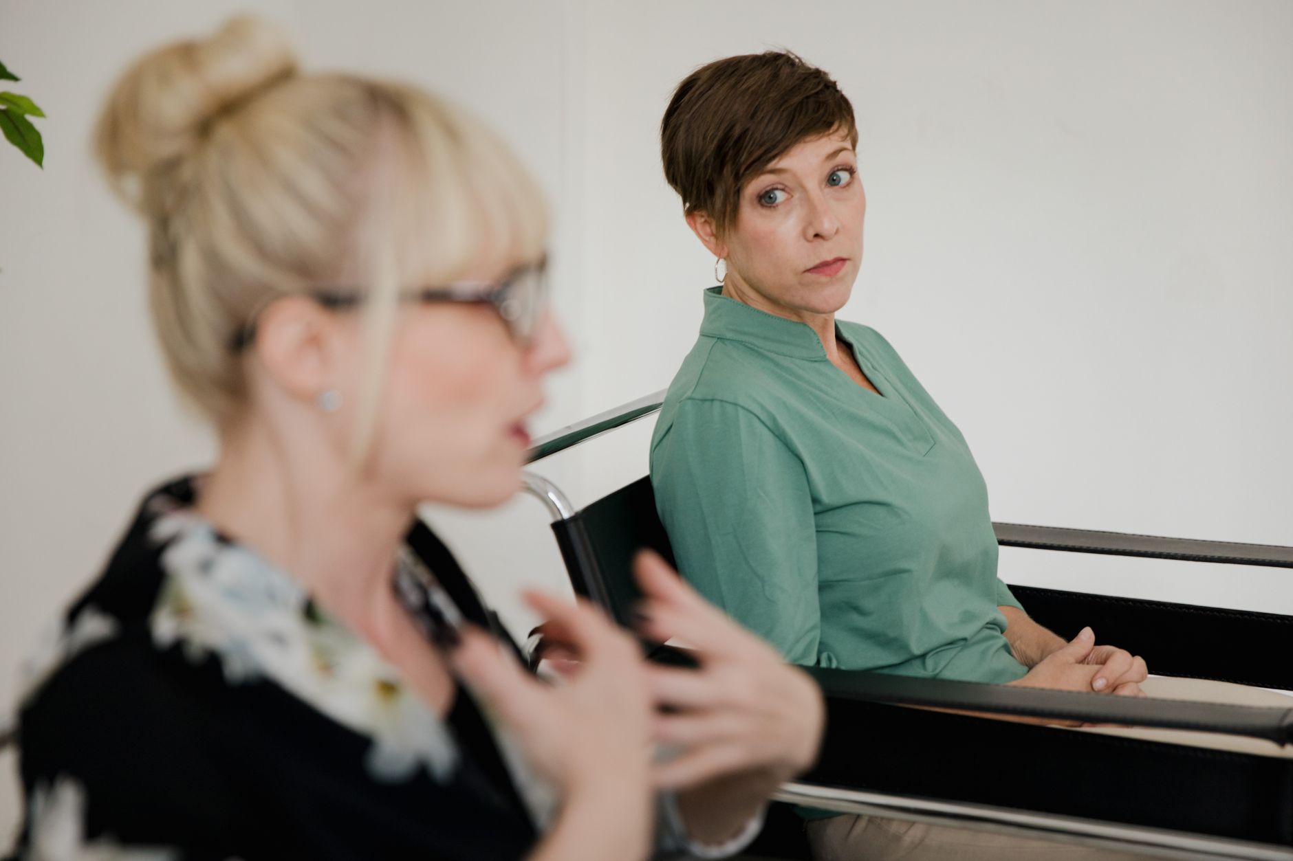 A person leaning forward with focused expression while another person speaks to them.