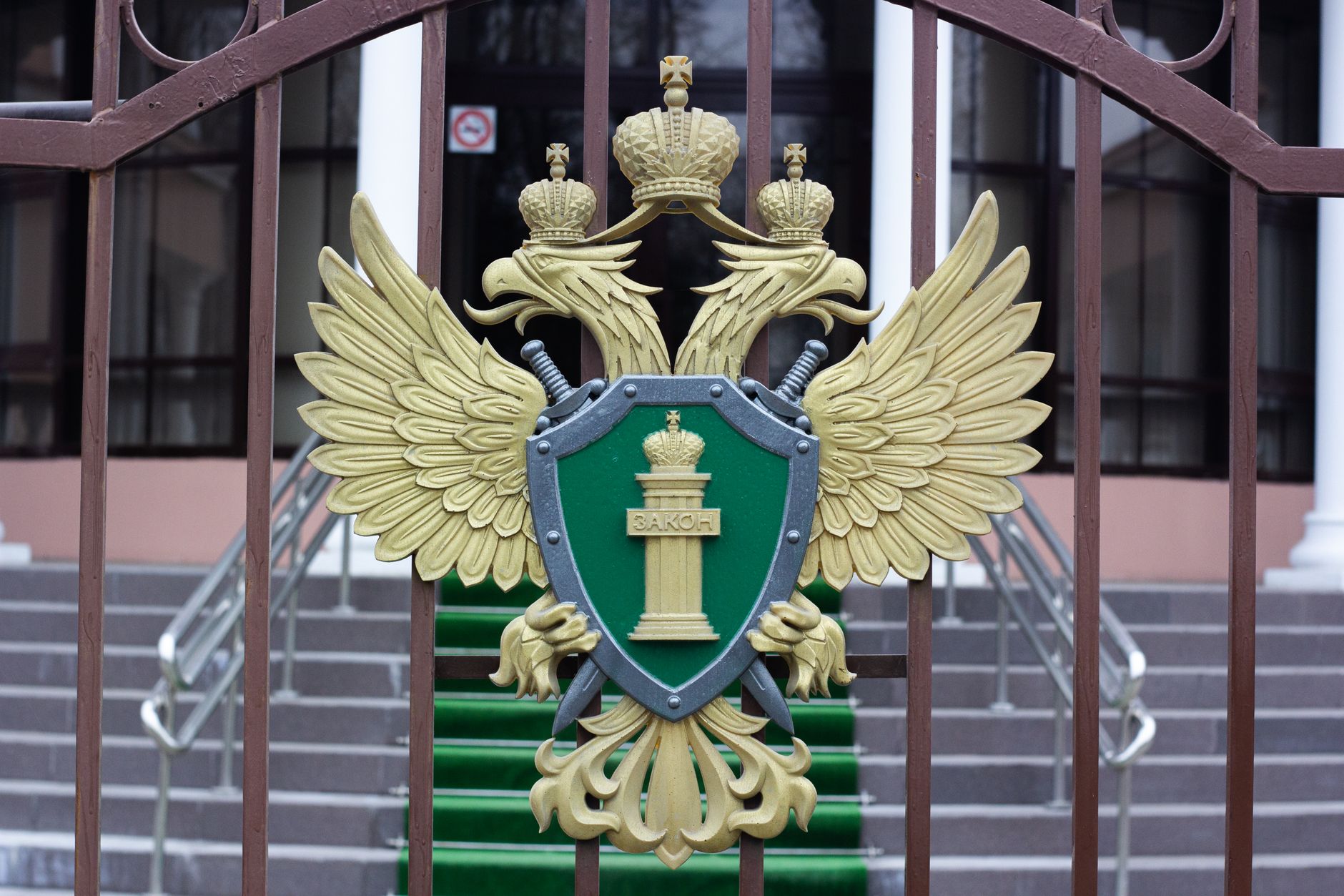 An ornate double-headed eagle emblem in gold on a dark red shield, formal and regal in style.