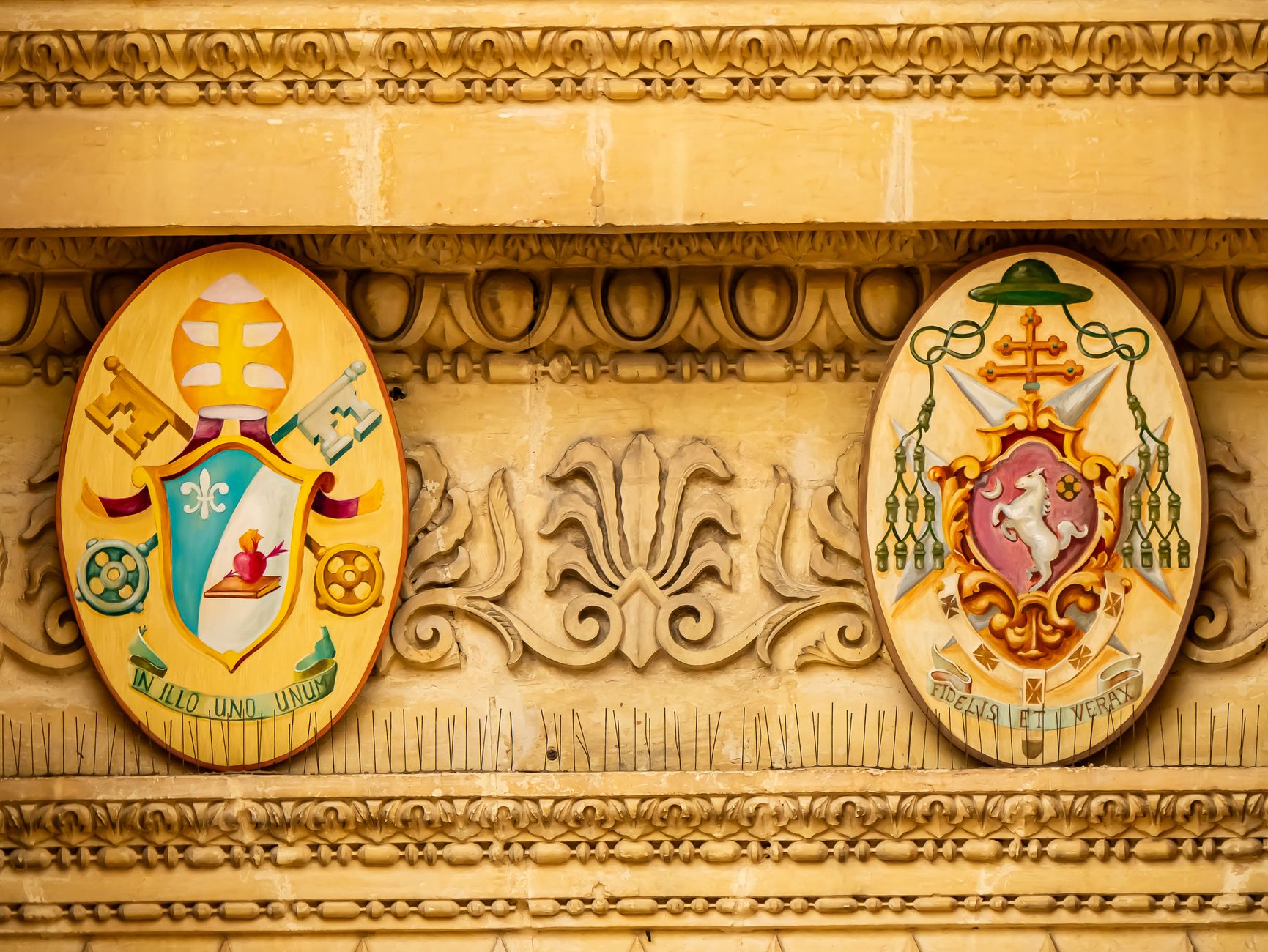 An ornate heraldic shield displaying intricate metalwork and symbolic designs in gold and deep red.