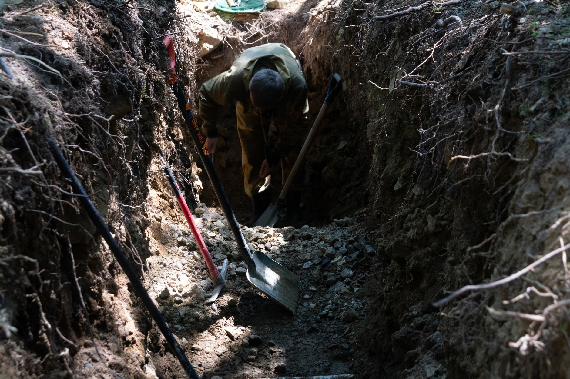 A figure with a shovel in soil as light fades, suggesting excavation of hidden truths.